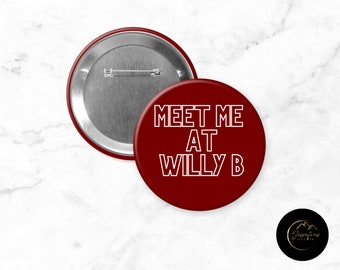 May include: A circular pin-back badge with a deep red background and white text that reads MEET ME AT WILLY B. The reverse side of the badge is metallic silver and features a horizontal pin mechanism for attachment to clothing or fabric items.