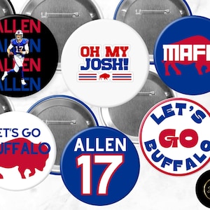 Puede incluir: Un conjunto de nueve botones redondos con varios diseños relacionados con el equipo de fútbol americano Buffalo Bills. Los botones están en los colores del equipo, azul y rojo, con texto e imágenes blancas. Algunos de los diseños incluyen el logotipo del equipo, el nombre del jugador "Allen" y la frase "Let's Go Buffalo".