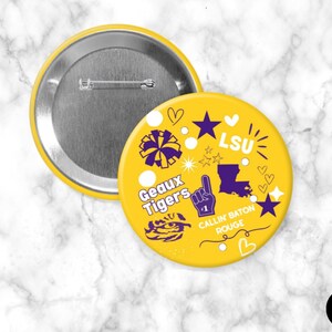 May include: A round yellow pinback button featuring purple and white graphics including a tiger mascot, a foam finger, the state of Louisiana, and text reading LSU, Geaux Tigers, and Callin Baton Rouge, with a metal pin mechanism on the back.