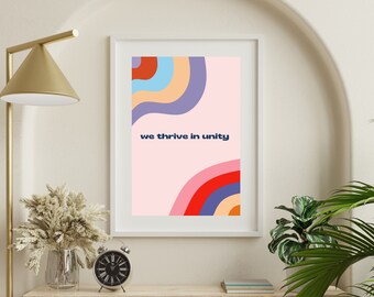 May include: A white framed print with a pink background and colorful abstract shapes. The text "we thrive in unity" is printed in blue on the print.