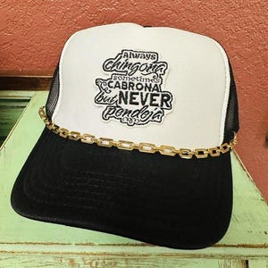 May include: Black and white trucker hat with a white mesh back. The hat has a black embroidered patch that says "Always Chingona Sometimes Cabrona But Never Pendeja".
