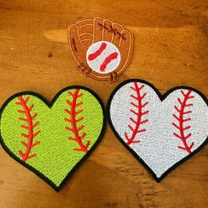 May include: Three embroidered patches in the shape of a baseball and two hearts. The baseball patch is brown with red stitching and a white baseball inside. One heart is green with red stitching and the other is white with red stitching.