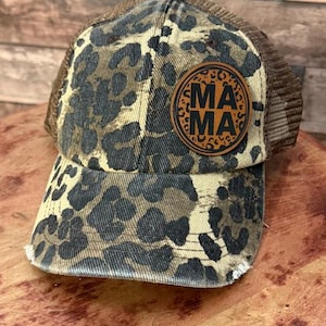 May include: A brown and black leopard print trucker hat with a brown leather patch that says "MAMA" in black letters.
