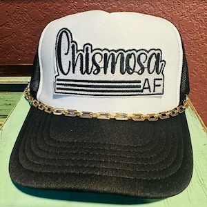 May include: White and black trucker hat with a black embroidered patch that says "Chismosa AF" on it. The hat has a gold chain around the brim.