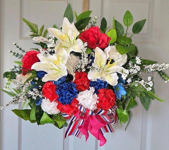 Patriotic Door Basket, this is a dark brown wicker basket carefully hand decorated with red, white, and blue faux flowers and lush greenery