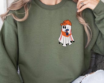 May include: Olive green sweatshirt featuring a baseball-themed ghost graphic. The ghost wears an orange baseball cap and holds a coffee cup. The graphic is a playful design, perfect for sports fans and those who enjoy Halloween.