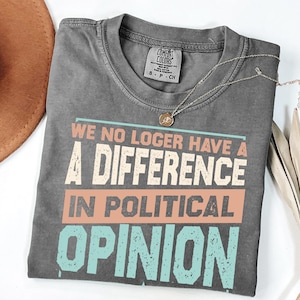 May include: A charcoal gray short-sleeve t-shirt with a distressed graphic print that reads: WE NO LOGER HAVE A DIFFERENCE IN POLITICAL OPINION. The text features a mix of peach and light blue colors with a vintage, weathered texture throughout the design.