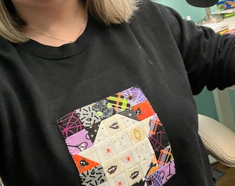 Può includere: Felpa nera con un design a patchwork colorato cucito sul davanti. Il design presenta una varietà di motivi a tema Halloween, tra cui ragni, pipistrelli e teschi.