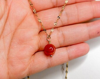 May include: A gold chain necklace with a red carnelian gemstone pendant.