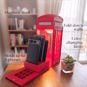 May include: A red phone box-shaped phone storage station with the text "TELEPHONES" on the front. Features include a magnetic roof, fold-down walls, a colour-changing lamp, and a base that holds up to 5 phones. The text "Screen-free meals" is visible.