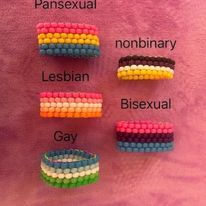 Può includere: Cinque braccialetti realizzati con piccole perline di plastica colorate disposte a strisce orizzontali. I braccialetti sono etichettati con il testo Pansexual, nonbinary, Lesbian, Bisexual e Gay, corrispondente al motivo cromatico.