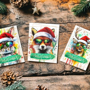 May include: Three Christmas cards featuring watercolor illustrations of a rabbit, fox, and deer, each wearing sunglasses and a Santa hat. The cards have the text "Merry Christmas" and are set against a rustic wooden background with pinecones and greenery.
