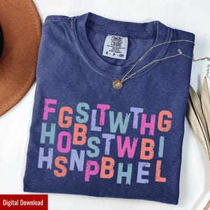 Può includere: Una maglietta Comfort Colors blu navy con testo colorato. Il testo è disposto in righe e include le lettere F, G, S, L, T, W, H, O, B, S, T, W, B, I, H, S, N, P, B, H, E, L. Una collana d'oro con un ciondolo è sulla maglietta.