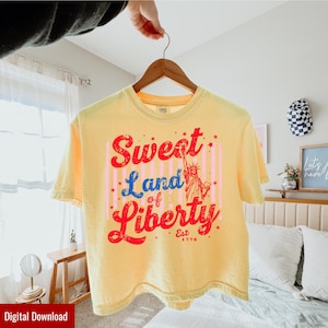 Könnte beinhalten: Hellgelbes T-Shirt mit dem Schriftzug "Sweet Land of Liberty" in Rot und Blau, mit der Freiheitsstatue. Das Shirt hat einen Vintage-Look und den Text "Est. 1776".