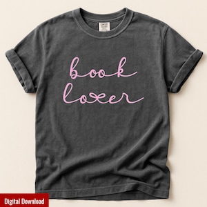 May include: Dark gray t-shirt with rolled-up sleeves. The shirt features the pink text "book lover" in a cursive font. The shirt is made of a soft material and has a classic crew neck.