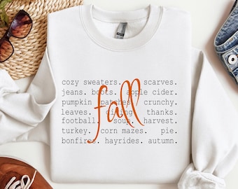 Pode incluir: Camisola branca com a palavra "fall" em escrita laranja, rodeada por palavras temáticas de outono como "cozy sweaters", "pumpkin patches" e "bonfires". A parte inferior da imagem inclui "Digital Download" e informações sobre o tipo de arquivo.
