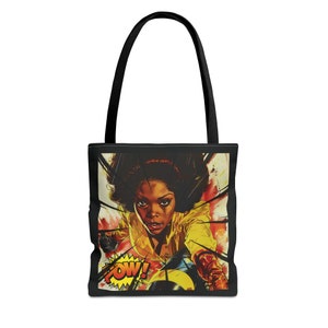 以下が含まれることがあります： 黒いトートバッグ。黄色いシャツを着た女性の漫画風イラストが描かれています。「POW！」という言葉が黄色と赤の吹き出しに入っています。バッグには黒いハンドルが付いています。