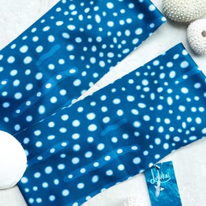 May include: A blue and white fabric headband with a whale shark pattern. The headband is folded in half and has a tag attached that says "Dulkai".
