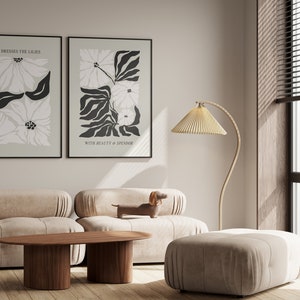 May include: Two framed floral art prints with black frames hang above a beige sofa. The prints feature abstract flower designs in black and white on a light green background. A wooden coffee table and a floor lamp are also in the room.