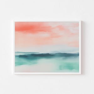 May include: A framed watercolor print featuring an abstract landscape. The artwork showcases a gradient of colors, with a coral-colored sky, a dark teal horizon, and a light teal foreground. The print is encased in a white frame.