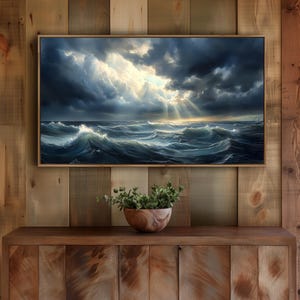 May include: A framed artwork depicts a dramatic seascape with turbulent waves under a stormy sky. Sunlight breaks through dark clouds, illuminating the ocean. The artwork is displayed above a wooden cabinet, with a wooden bowl of greenery in front.