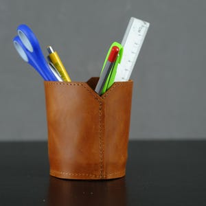 以下が含まれることがあります： 定規、ハサミ、ペンが入った茶色の革製のデスクオーガナイザー