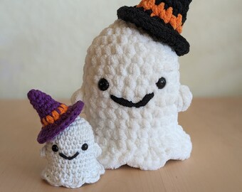 Op de afbeelding: Twee gehaakte spookversieringen met glimlachende gezichten. Het grotere spook draagt een zwarte heksenhoed met oranje rand. Het kleinere spook draagt een paarse heksenhoed met oranje rand.