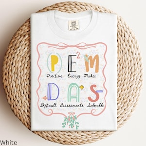 May include: White t-shirt with a colorful graphic that reads "POEM DAS" with the words "Positive Energy Makes Difficult Assessments Solvable". The design is framed with a pink border and floral accents.