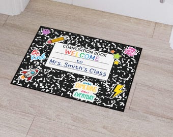 May include: Black and white welcome mat with a composition book design. It says "Composition Book Welcome to Mrs. Smith's Class". There are colorful stickers with phrases like "Be Kind", "You Got This", and "Learn Something New Everyday".