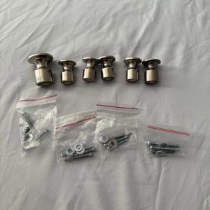 May include: A set of eight silver-toned cabinet knobs with a mushroom-shaped design. The knobs are arranged in a row above four small plastic bags containing screws and washers, likely for installation. The hardware is displayed on a white surface.