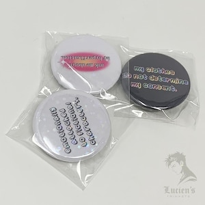 May include: Three round pinback buttons in clear plastic packaging. One white button has the text "emotionally attached to fictional characters." Another white button says "ask me about my hyperfixation." A black button reads "my clothes do not determine my consent."