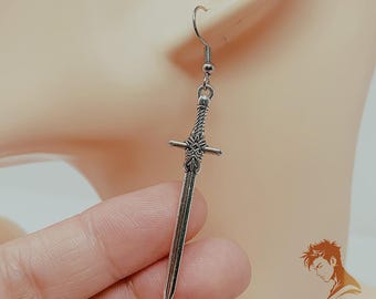 May include: A silver-colored sword-shaped earring with intricate detailing. The earring features a hook for the ear and a decorative handle. The blade is long and pointed. The earring is held up to an ear. The logo "Lucien's Trinkets" is in the bottom right corner.