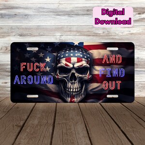 May include: A black license plate featuring a skull wearing a patriotic bandana, set against an American flag backdrop. The plate has the words "FUCK AROUND AND FIND OUT" in red and blue neon-style lettering.