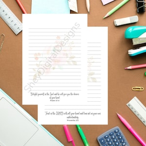 May include: Two sheets of lined paper featuring floral designs and inspirational quotes. The text includes "Delight yourself in the Lord" and "Trust in the Lord". Stationery items such as pens, pencils, and a stapler surround the paper.