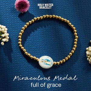 May include: Gold beaded bracelet with a round, white pendant featuring a religious image in blue and gold. The bracelet is on a dark blue surface, with text that reads "Holy Water Bracelet" and "Miraculous Medal full of grace".
