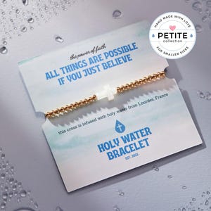 May include: A gold beaded bracelet with a white cross charm. The card reads "the power of faith ALL THINGS ARE POSSIBLE IF YOU JUST BELIEVE" and "HOLY WATER BRACELET EST. 2023".