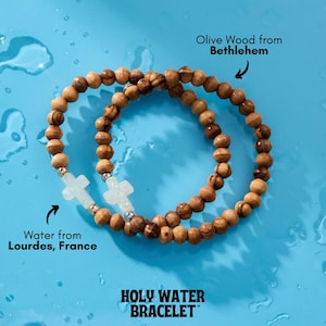 May include: Two bracelets made of olive wood beads from Bethlehem, with a white cross charm. The bracelets are on a blue background with water droplets. The text "HOLY WATER BRACELET™" is at the bottom of the image. The text "Water from Lourdes, France" is on the left side of the image. The text "Olive Wood from Bethlehem" is on the right side of the image.