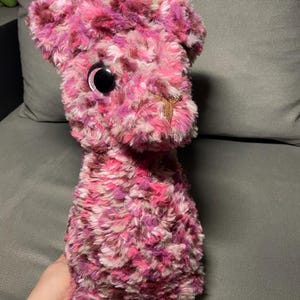 May include: A pink and white plush toy with large black eyes. The toy is shaped like a llama and has a brown nose.