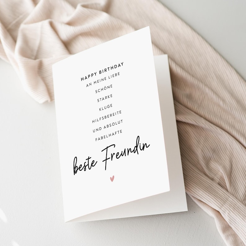 May include: A white greeting card with the text "HAPPY BIRTHDAY" and a list of positive adjectives in German. The card also features the words "beste Freundin" in cursive and a small pink heart.