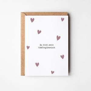 May include: A white greeting card with scattered mauve hearts and the German text "du bist mein Lieblingsmensch" (you are my favorite person). The card is inside a brown envelope.