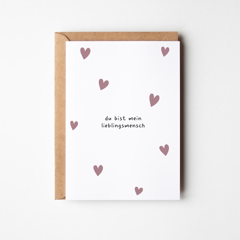 May include: A white greeting card with scattered mauve hearts and the German text "du bist mein Lieblingsmensch" (you are my favorite person). The card is inside a brown envelope.