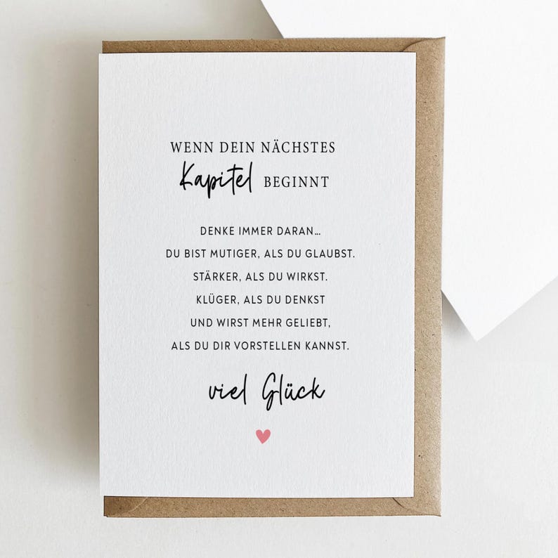 May include: A greeting card with a white interior and a brown envelope. The card features black text, including "WENN DEIN N&Auml;CHSTES Kapitel BEGINNT" and other motivational phrases. A small pink heart is at the bottom.