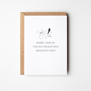 Puede incluir: Tarjeta blanca con ilustraci&oacute;n de una cig&uuml;e&ntilde;a llevando un paquete, con el texto en alem&aacute;n "DANKE, DASS DU UNS AUF DIESEM WEG BEGLEITET HAST." La tarjeta est&aacute; dentro de un sobre marr&oacute;n, ideal para un anuncio de nacimiento.
