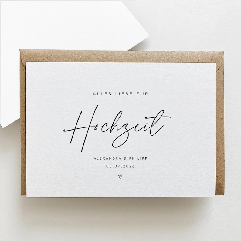 Puede incluir: Una tarjeta blanca con las palabras "ALLES LIEBE ZUR Hochzeit" en escritura negra, con los nombres "ALEXANDRA & PHILIPP" y la fecha "05.07.2026" debajo. La tarjeta est&aacute; dentro de un sobre marr&oacute;n.