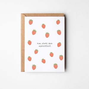 Könnte beinhalten: Eine weiße Grußkarte mit einem wiederkehrenden Muster aus kleinen roten Erdbeeren mit grünen Blättern. In der Mitte der Karte steht der schwarze Text "hier steht dein wunschtext". Die Karte steckt in einem braunen Kraftpapierumschlag.