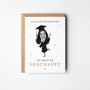 Könnte beinhalten: Eine weiße Grußkarte mit einer Karikatur einer Absolventin in schwarzem Talar und Doktorhut, die ein Diplom hält. Der Text lautet ALLES GUTE ZUM ABSCHLUSS und DU HAST ES GESCHAFFT. Kleine goldene Herzen und Sterne sind auf der Karte verteilt.