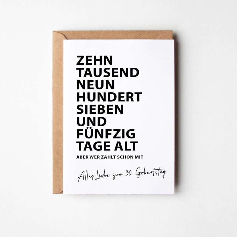 K&ouml;nnte beinhalten: Eine wei&szlig;e Gru&szlig;karte mit schwarzem Text in einem braunen Umschlag. Auf der Karte steht "ZEHN TAUSEND NEUN HUNDERT SIEBEN UND F&Uuml;NFZIG TAGE ALT" und "Alles Liebe zum 30. Geburtstag."
