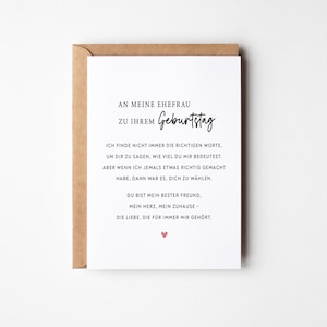 May include: A white greeting card with German text, presented in a brown envelope. The card's message is a birthday wish to a wife, with a small pink heart at the bottom. The card's text is in black, with the word "Geburtstag" in a handwritten style.