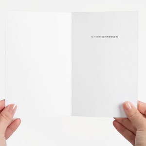 May include: A blank white card with the text "Ich bin schwanger!" printed in black on the right side.