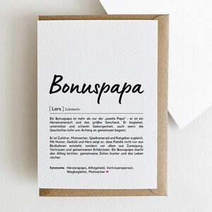 May include: A greeting card with the word "Bonuspapa" in large, black script. The card is white with text in German, and is inside a brown envelope. The card's text describes the meaning of "Bonuspapa".